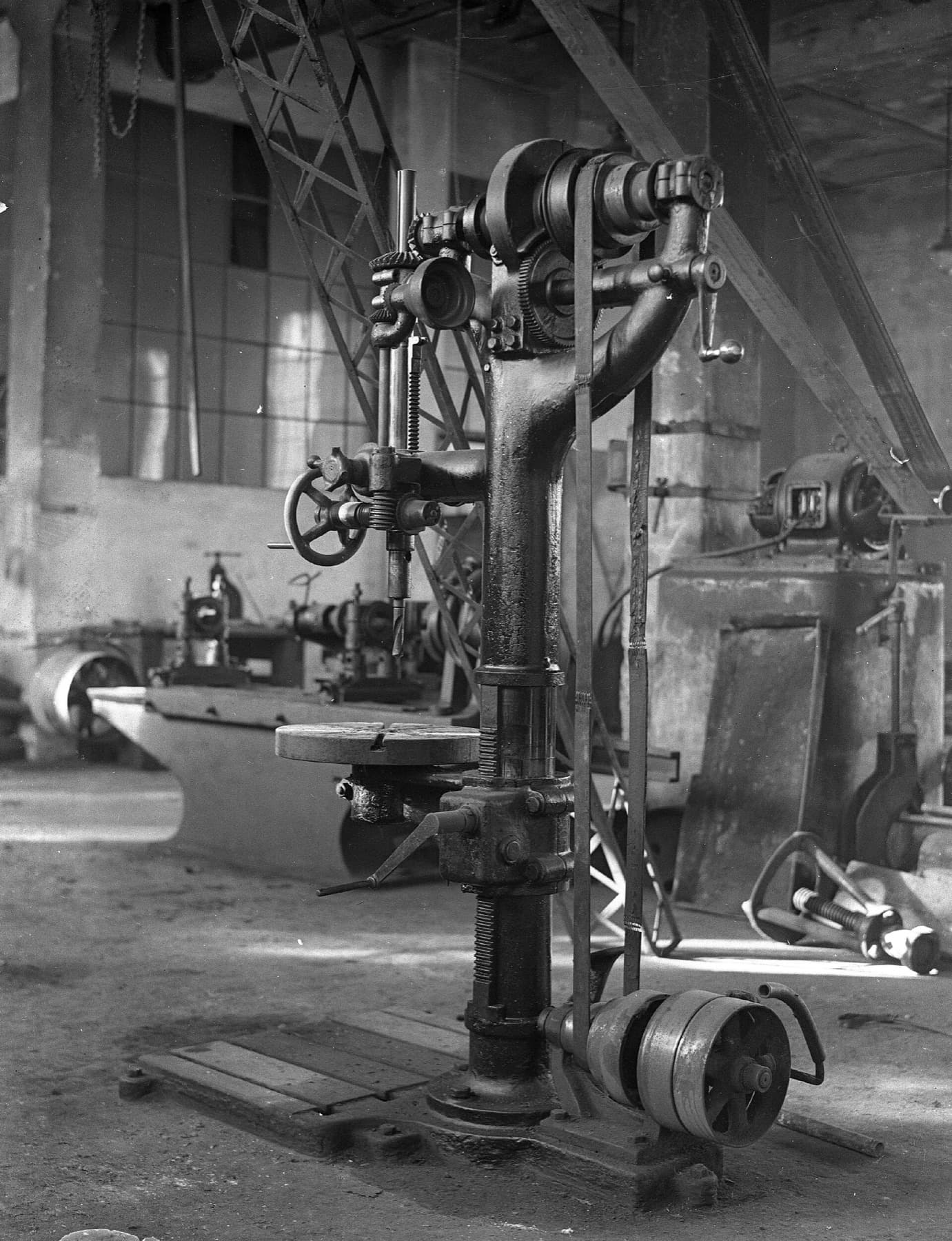 A radial boring machine on a workshop floor around 1916, its drive pulley at the base and more belt-driven machines behind it.